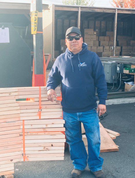A man standing next to stacks of wood.